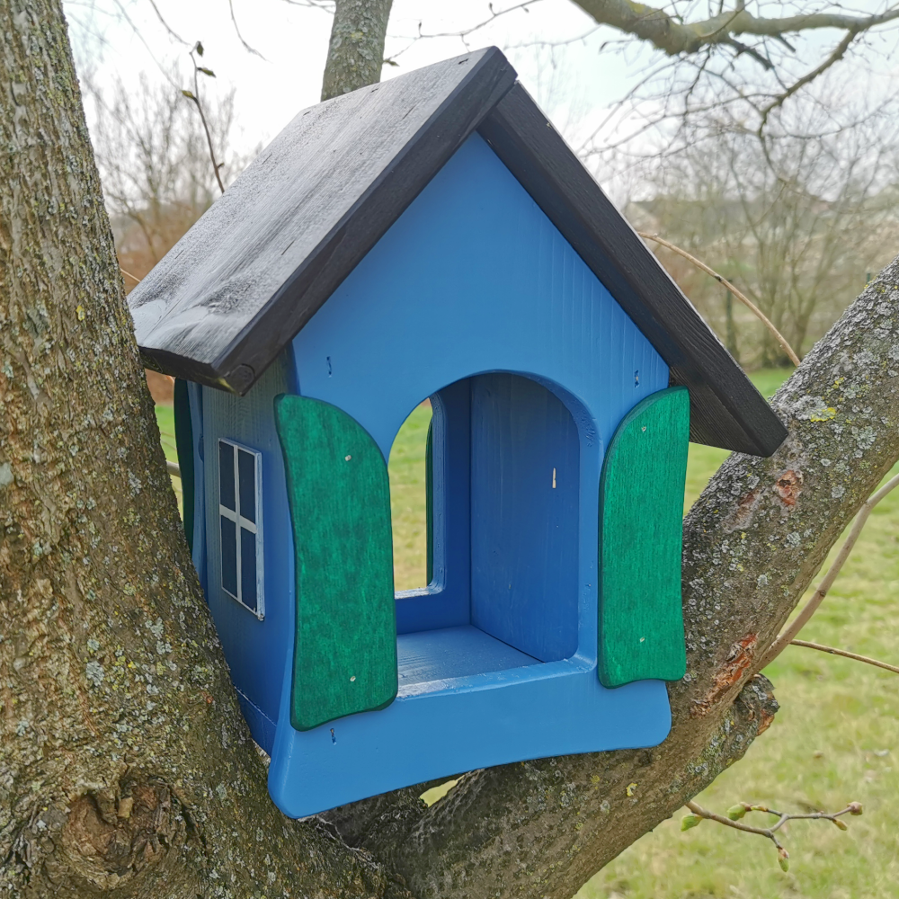 blaues Vogelhäuschen in Baum vor Wiese