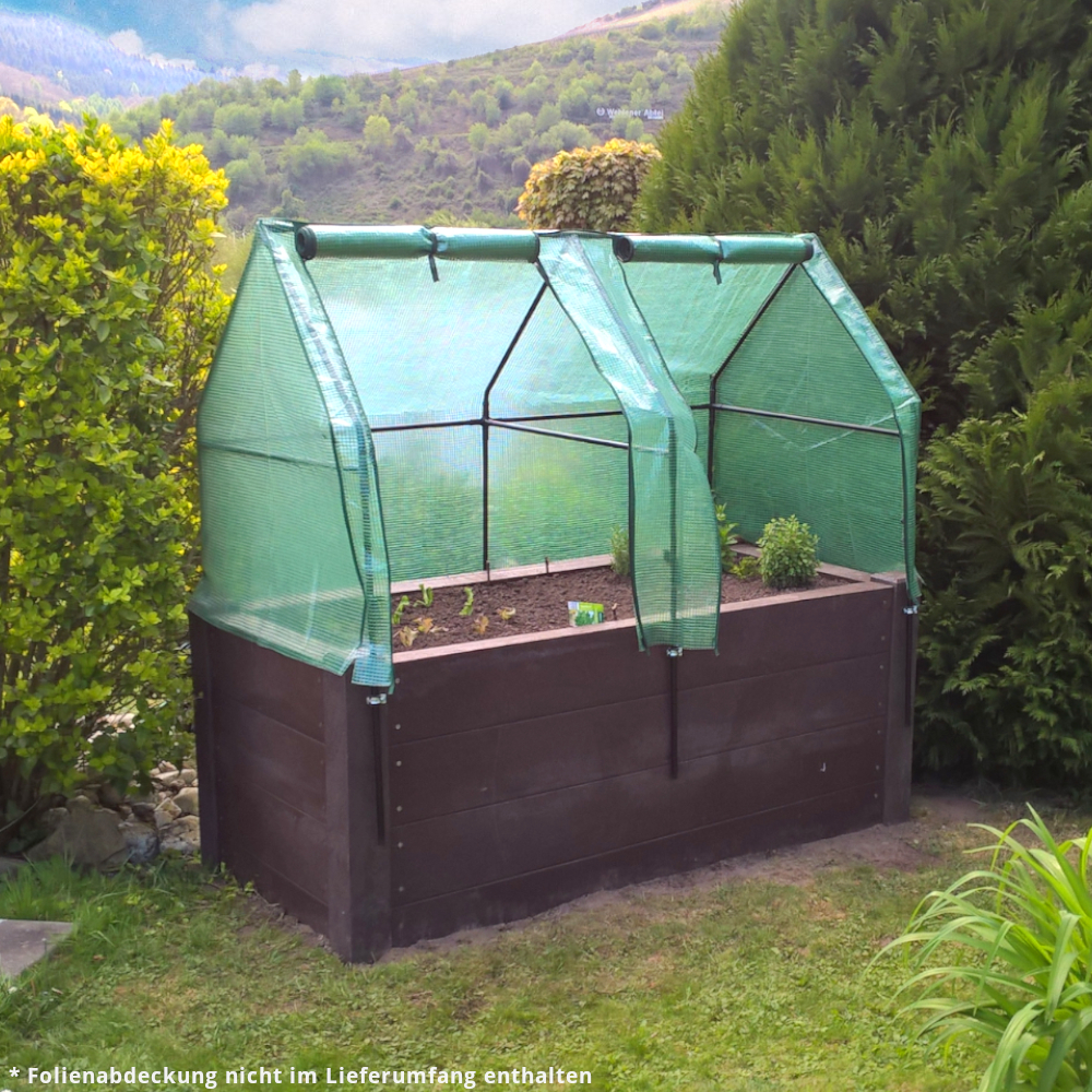 braunes Hochbeet mit zarten neuen Pflänzchen und Überdachung auf Wiese vor Berg