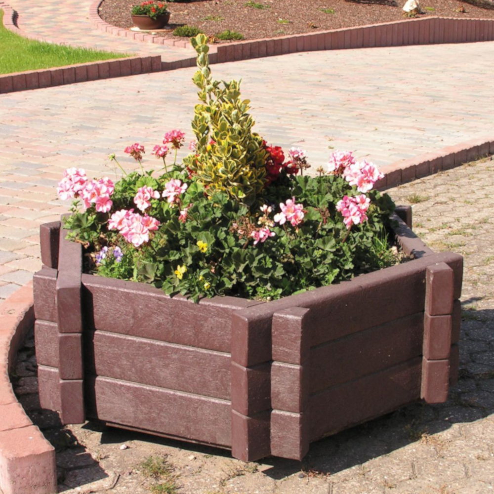 sechseckiger brauner Blumenkübel mit blühenden Pflanzen auf Gehweg