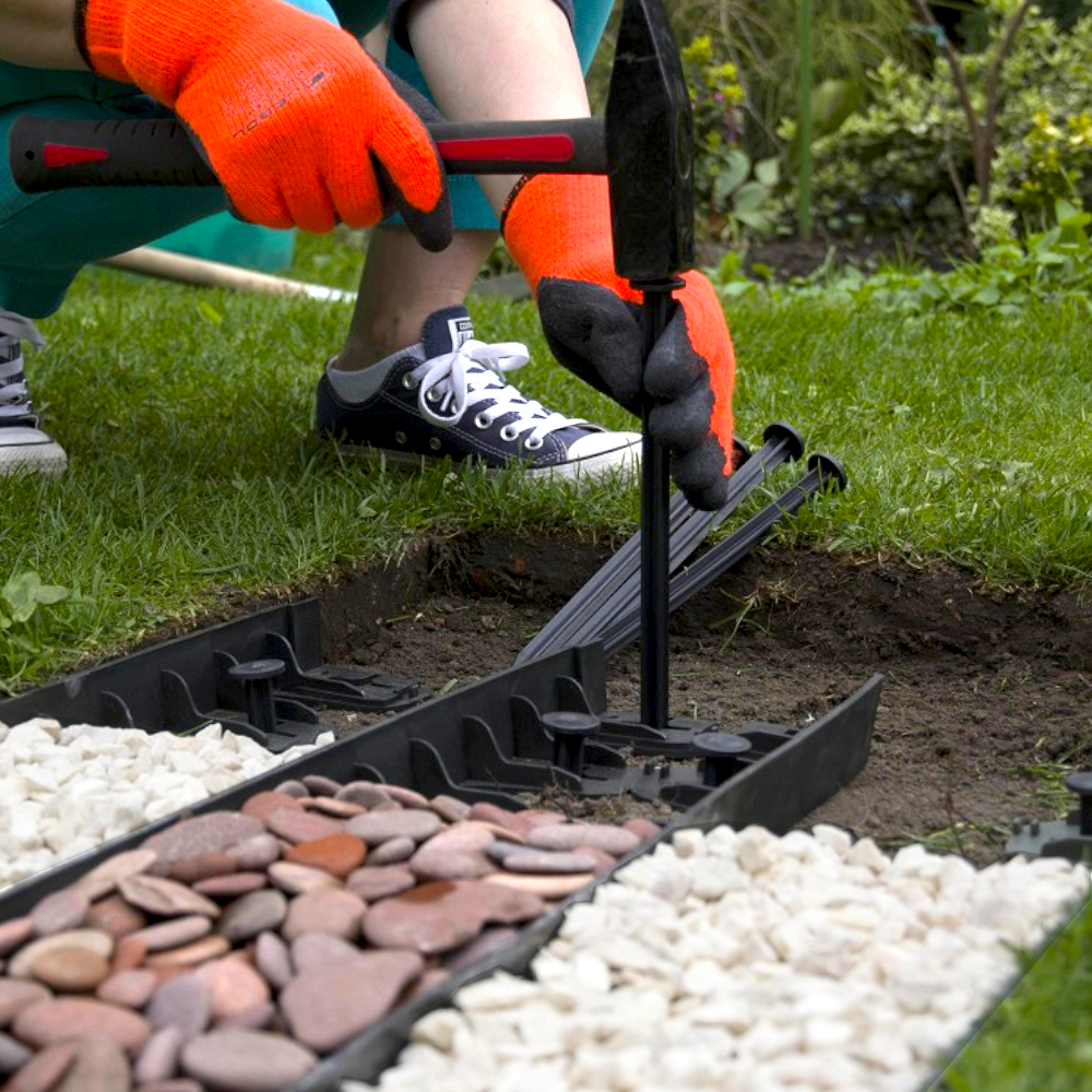 schwarzer Plastiknagel wird in gerade Plastikbahn eingeschlagen vor Wiese