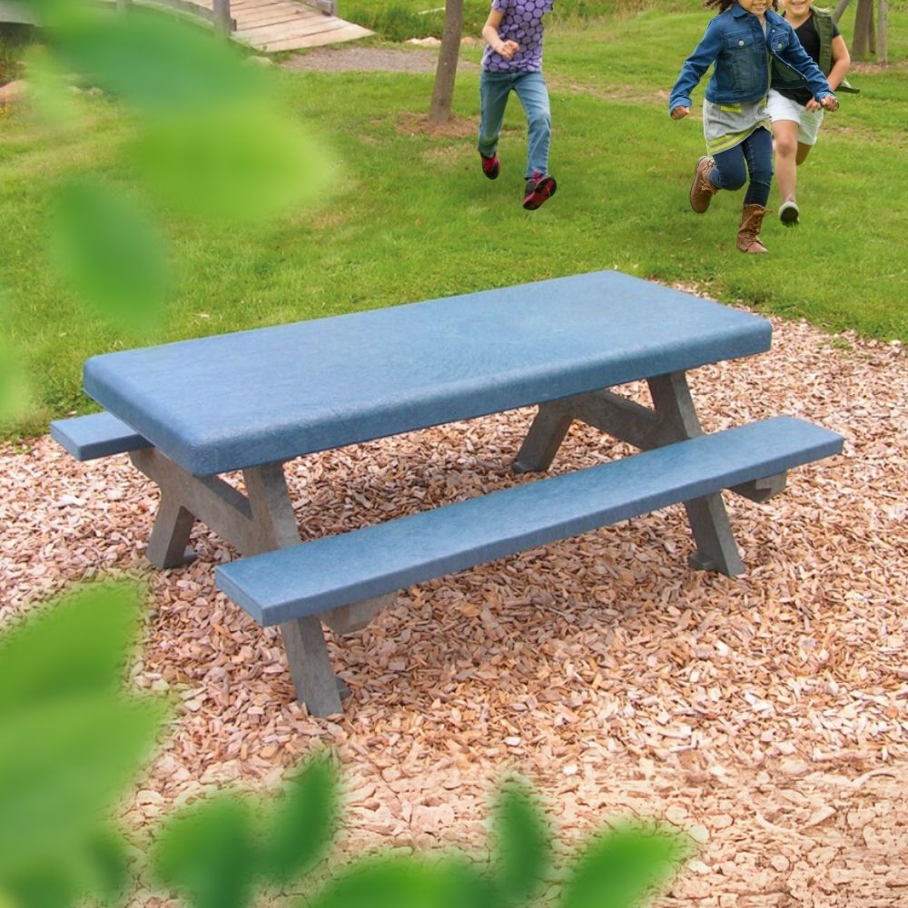 grau-blaue Kindersitzgruppe aus Recyclingkunststoff auf Holzpellets vor Wiese mit spielenden Kindern