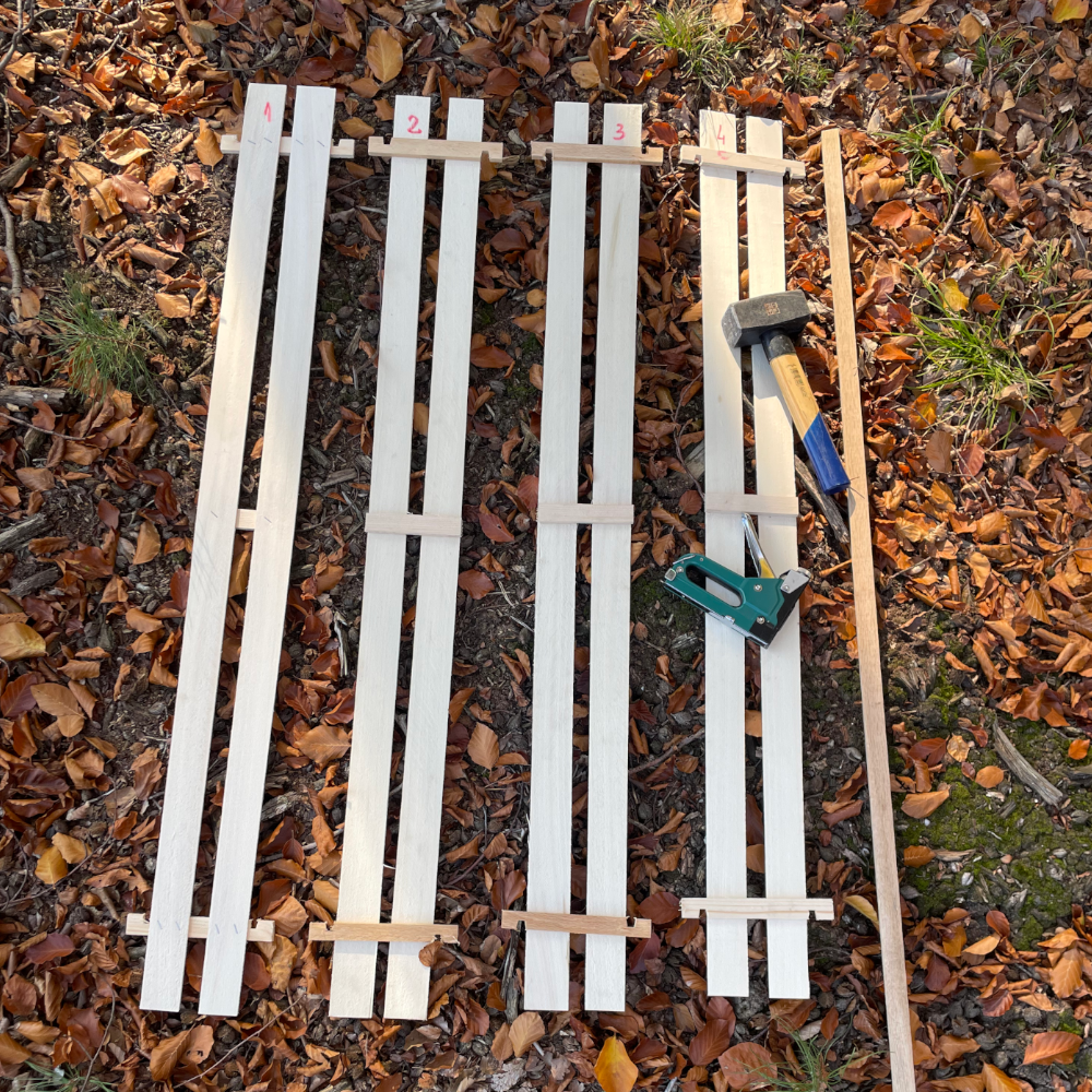 die 4 Seiten der Pure Nature Holz-Wuchshülle und ein Hartholzpfahl auf Waldboden ausgelegt