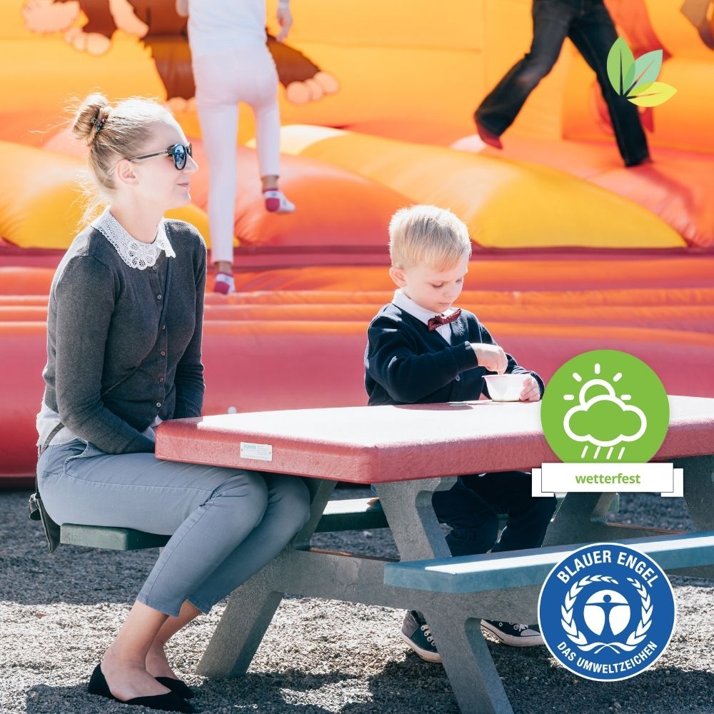 Mutter und Sohn sitzend auf roter Kindersitzgruppe vor Hüpfburg