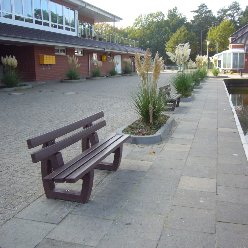 eine braune aus Parkbank aus Recyclingkunststoff steht auf einer Promenade