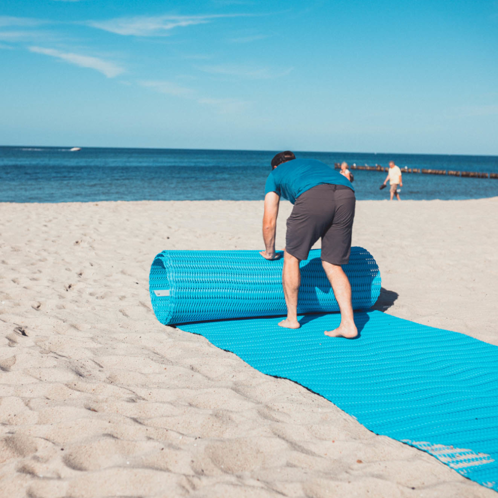 Blaue Sandmatte wird am Strand ausgerollt.