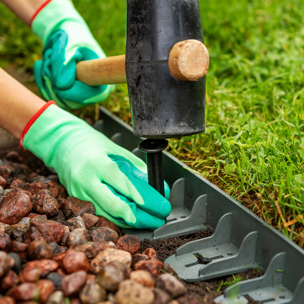 schwarzer Plastiknagel wird in gerade Plastikbahn eingeschlagen vor Wiese