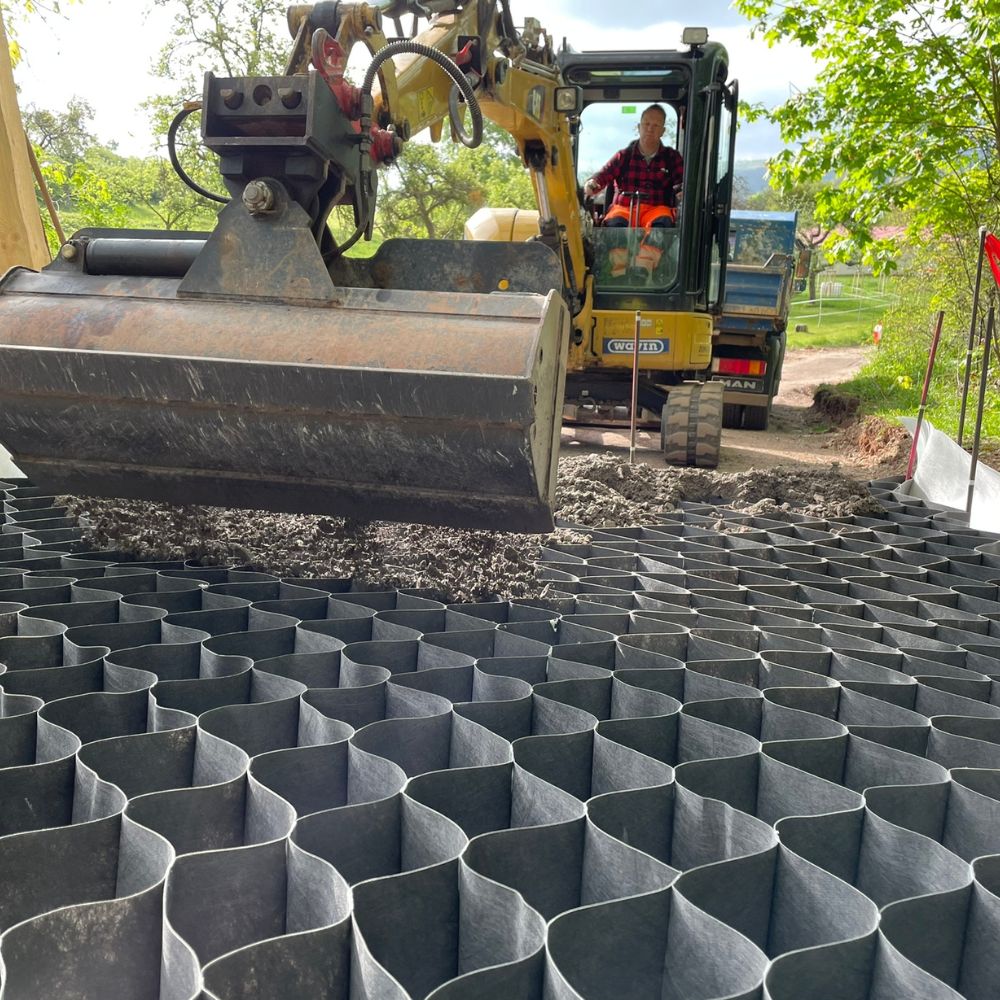 Ein Bagger verlegt Material auf eine strukturierte Oberfläche aus schwarz-grauem Wurzelbrücken.