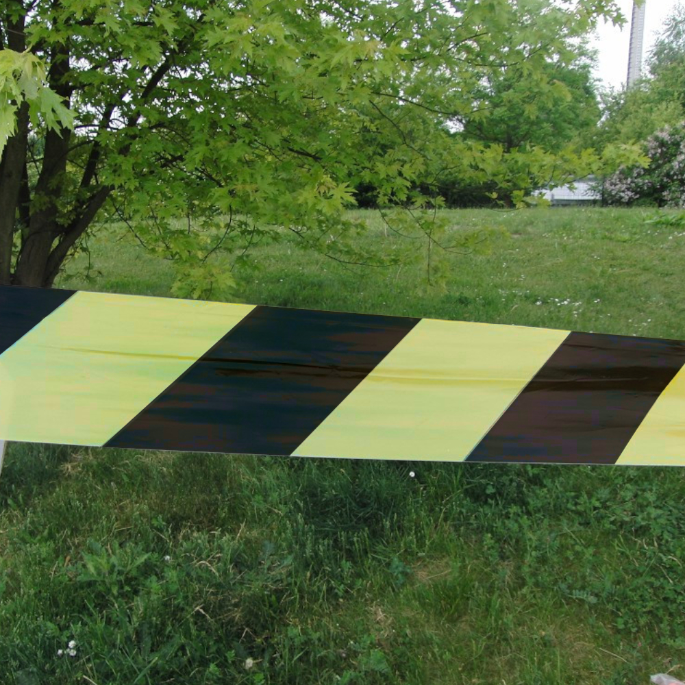 schwarz / gelbes Absperrband vor Baum auf Rasen