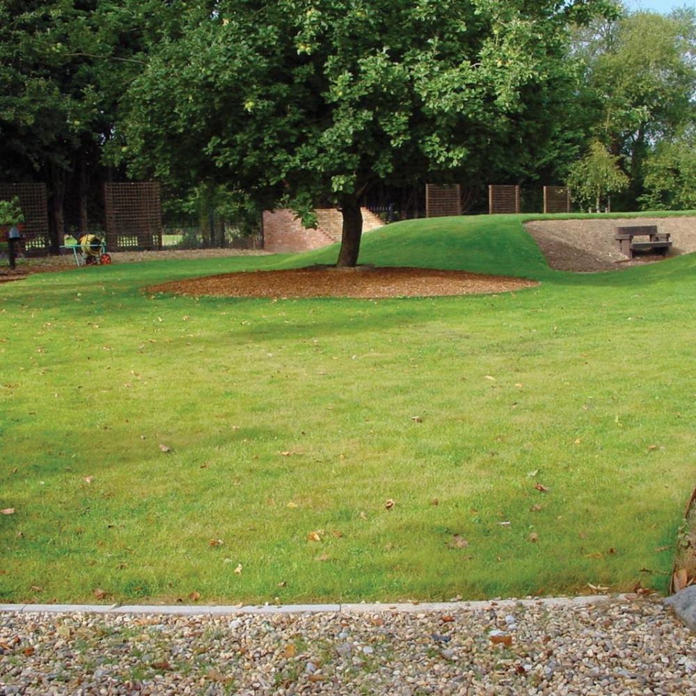 braune Kiesfläche im Vordergrund vor Wiesenfläche im Hintergrund