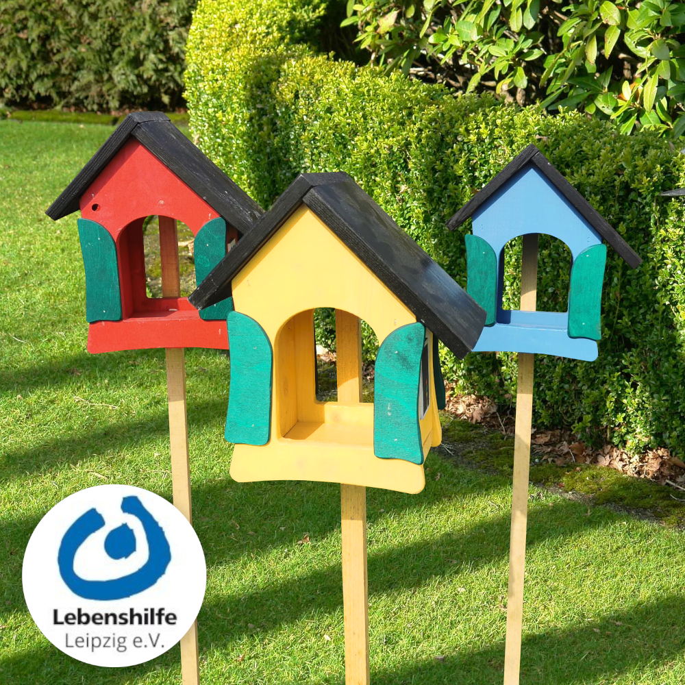 Bunte Vogelhäuschen aus Holz, handgefertigte Unikate aus WfbM-Produktion, 25 x 19 x 30cm bunte Vogelhäuschen auf Stab gesteckt auf Wiese vor Busch von der Lebenshilfe Leipzig e.V.