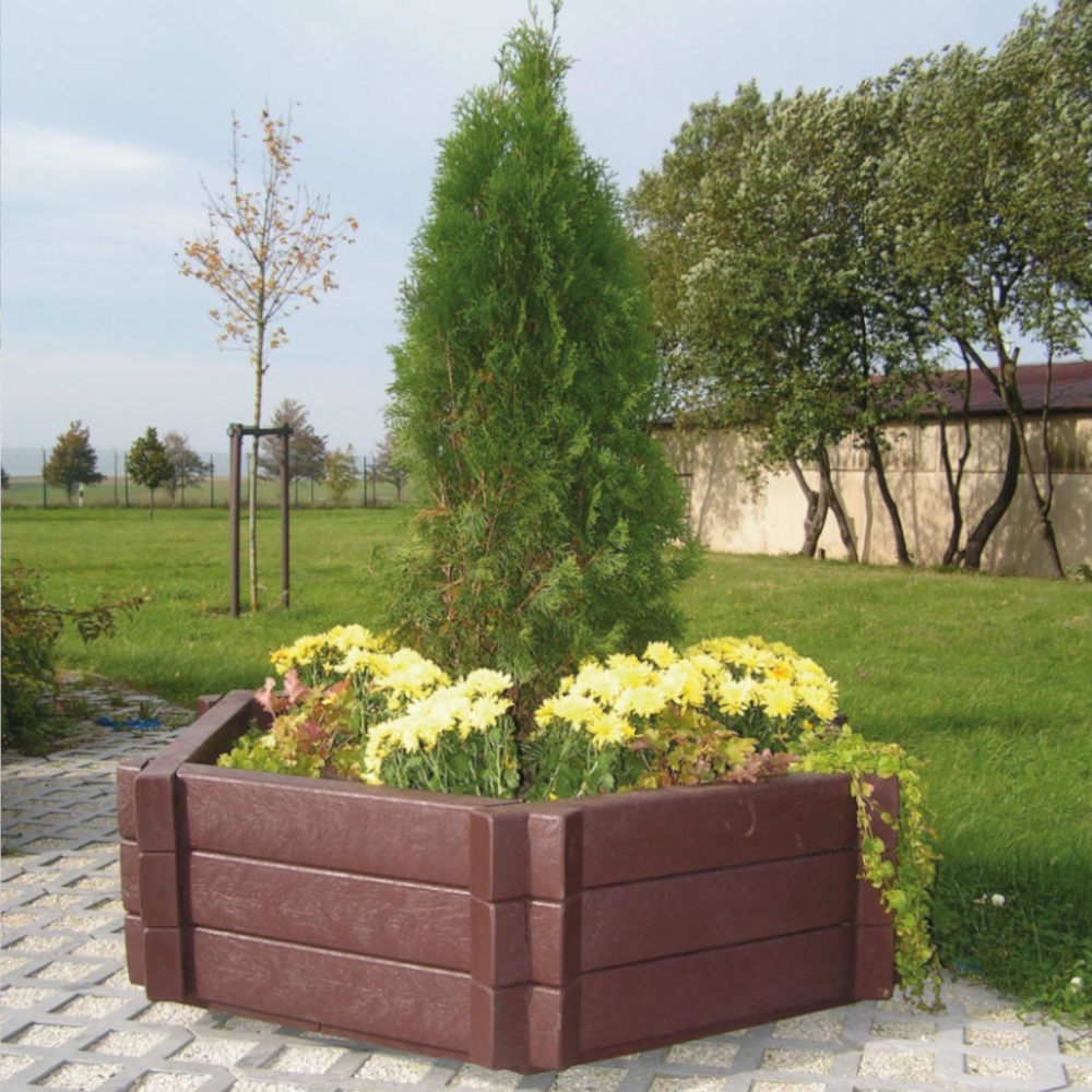 brauner sechseckiger Blumenkübel mit Bepflanzung auf Rasengittersteinen vor Wiese und Mauer