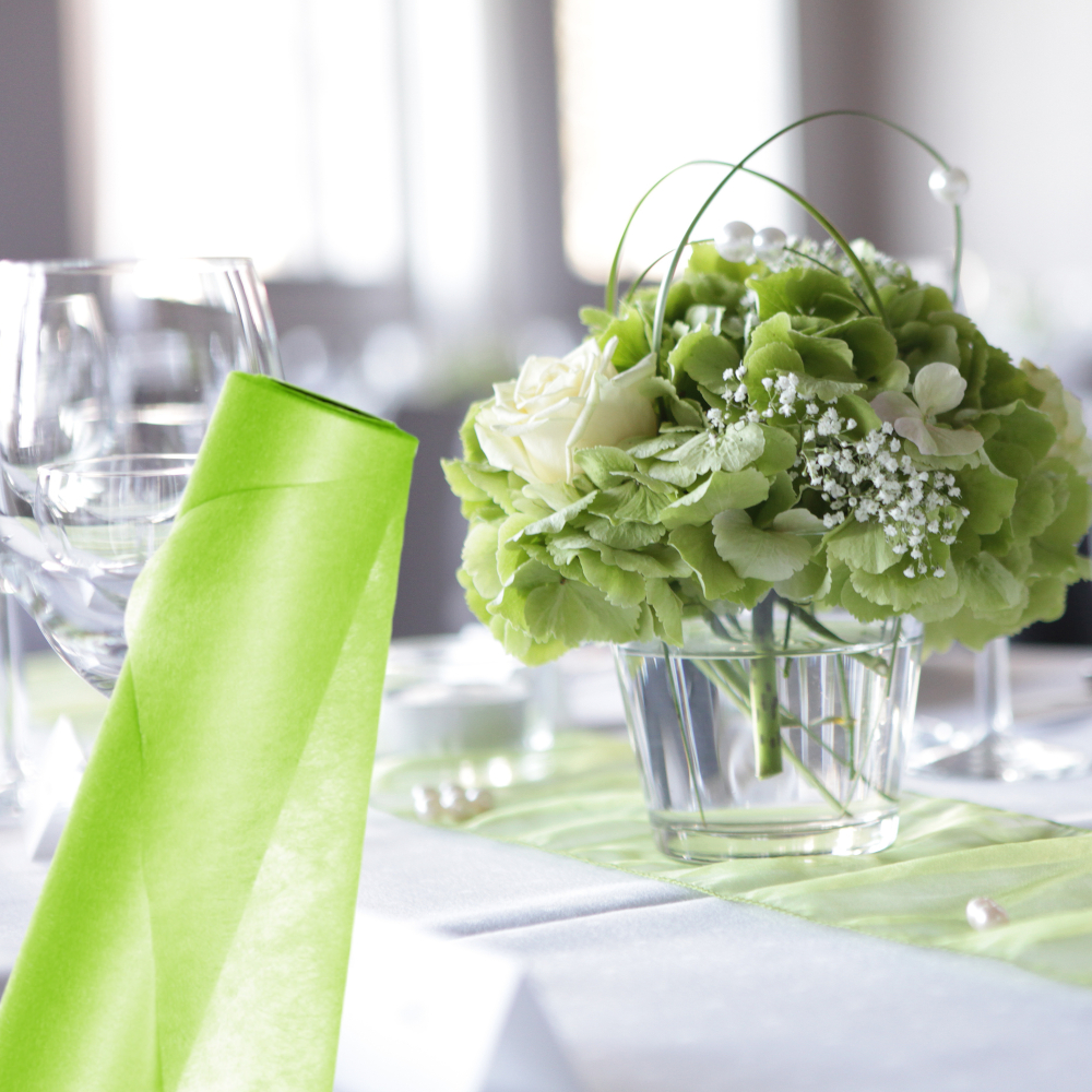 grüne Vliesrolle vor weiß geschmücktem Tisch mit Blumenstrauß