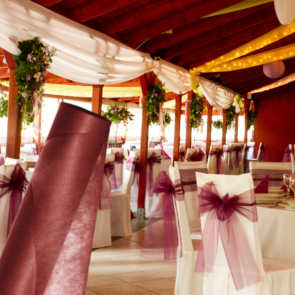 rote Vliesrolle vor geschmückter Halle mit weißen Stühlen versehen mit roter Schleife aus Vlies
