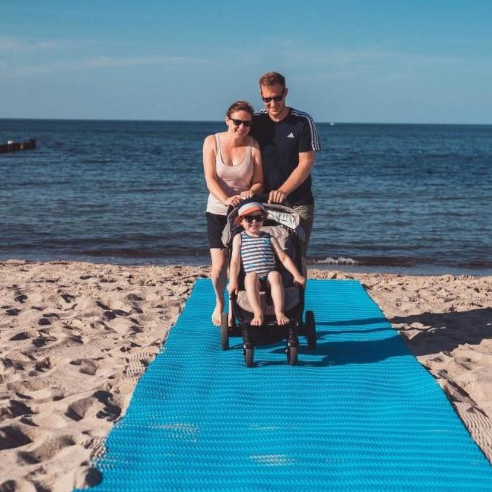 Familie mit Kinderwagen auf blauer Sandmatte am Strand.