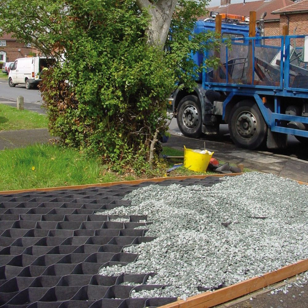 TERRAM Geozellen Ein Baustellenbereich mit einem Gitter aus schwarzem Material und Kies, sowie einem Lkw im Hintergrund.