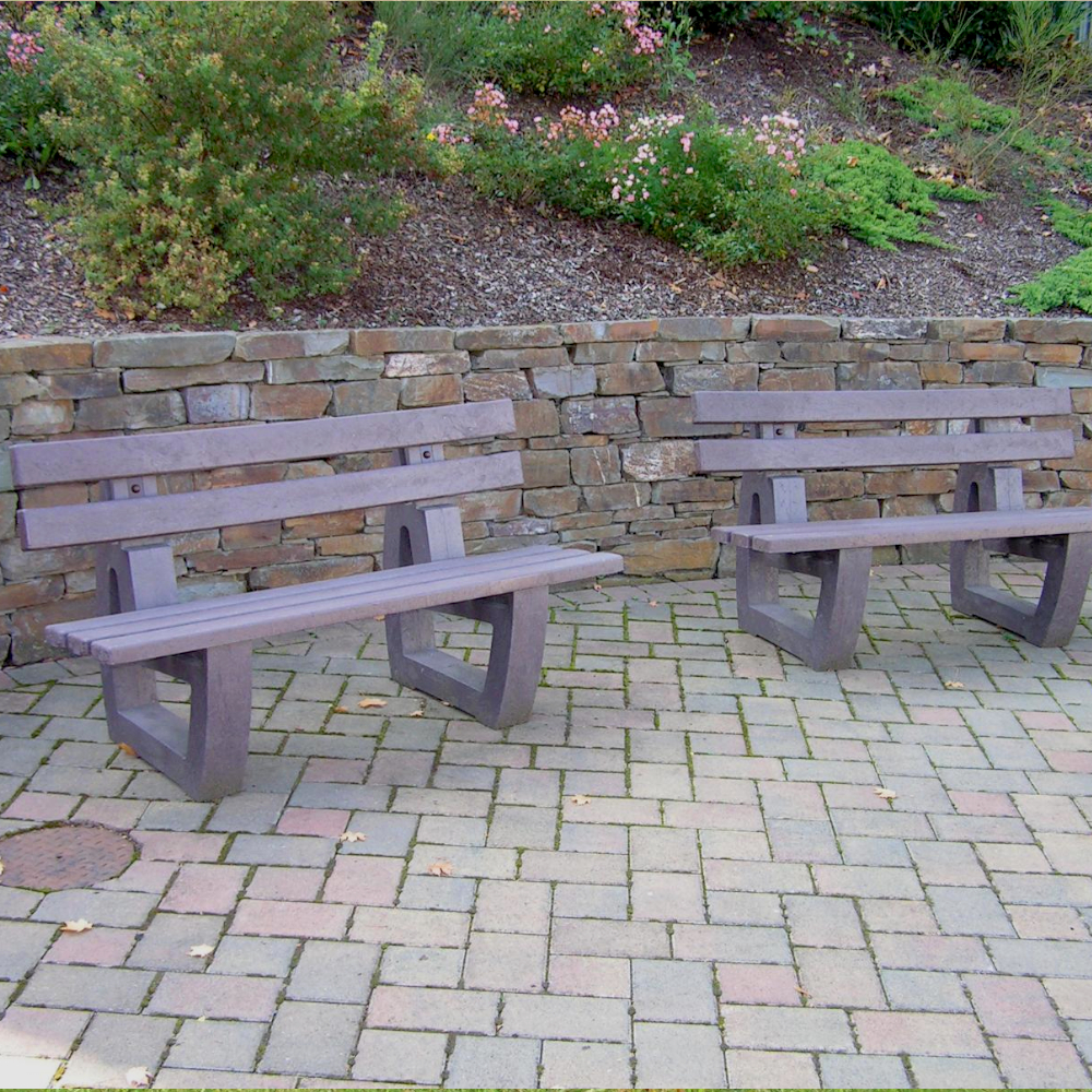 zwei braune Parkbänke aus Recyclingkunststoff stehen nebeneinander vor einer Böschung