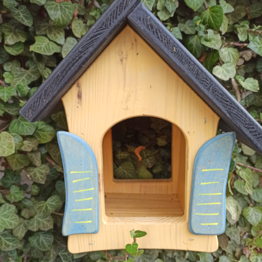 gelbes Vogelhäuschen vor Busch